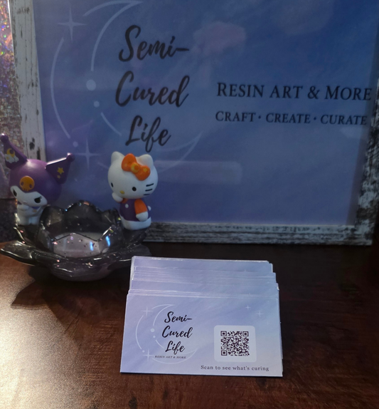 tack of Semi-Cured Life business cards with a celestial logo and QR code, printed on glossy photo paper and layered onto premium white cardstock, displayed beside small character figurines.